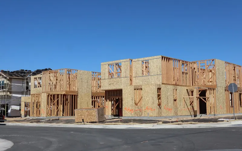 Timber-framed houses under construction, with sheathed walls, against a clear blue sky